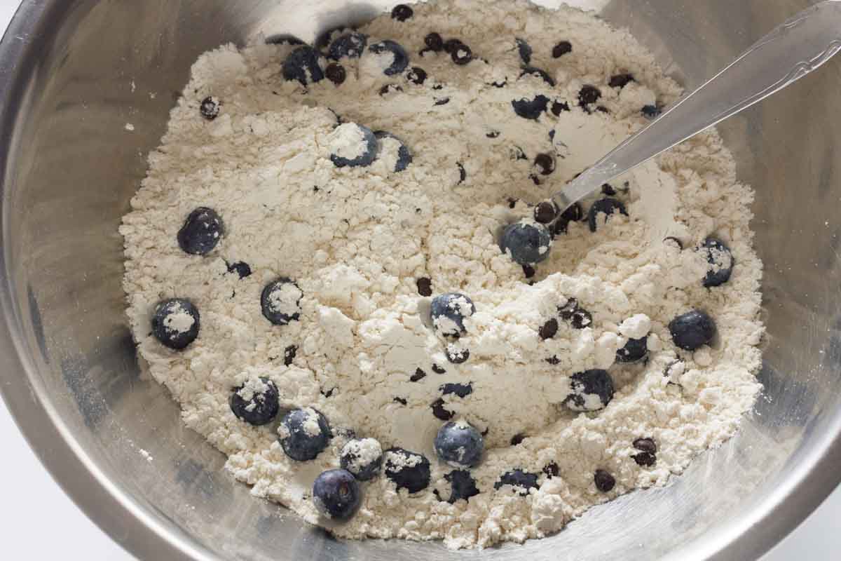 Stirring blueberries and chocolate chips into flour and other dry ingredients with a spoon.