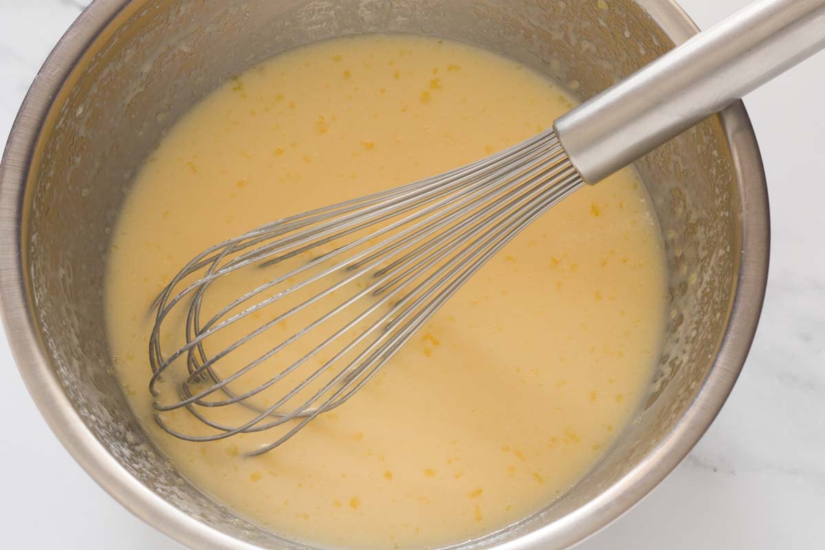 Whisking togethre eggs, milk, oil, butter and sugar in a mixing bowl.