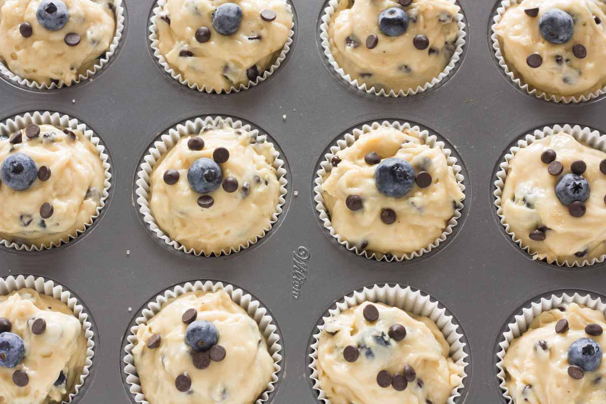 A cupcake pan lined with muffin cups and filled with blueberry chocolate chip muffin batter.