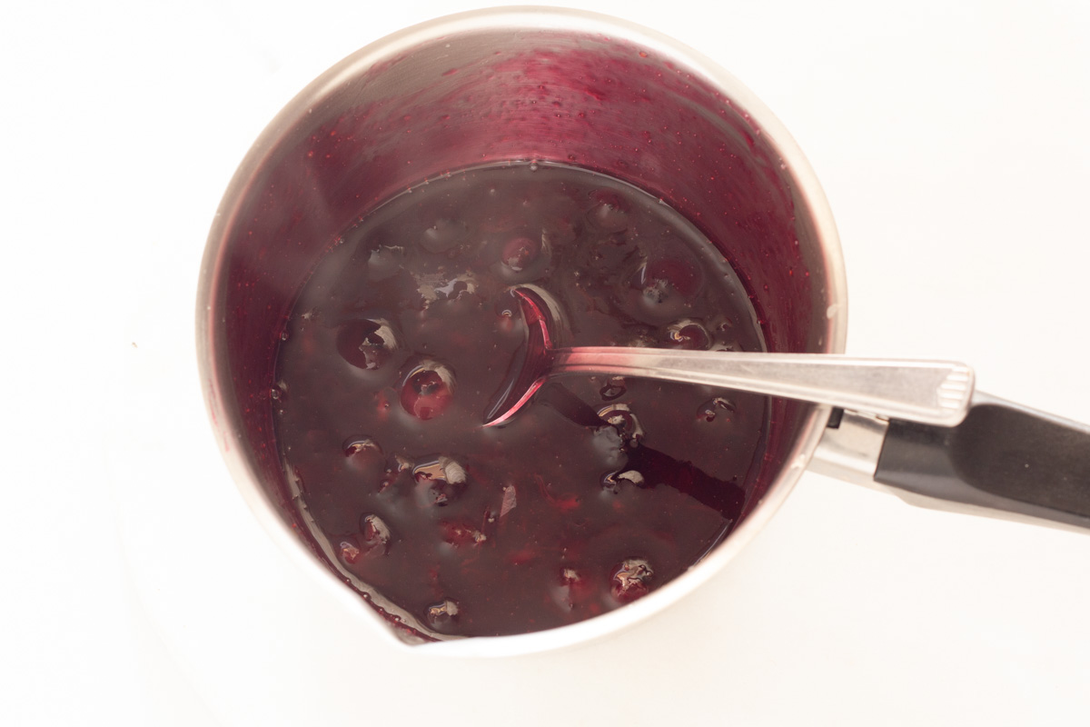 Cooked blueberry sauce in a small saucepan with a spoon.