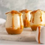 Three serving glasses of Dulce de leche mousse on a white marble surface with dulce de leche dripping on top.