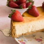 A slice of New York cheesecake on a cake server with strawberries on top.