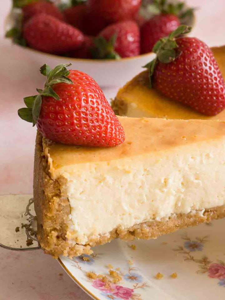 A slice of New York cheesecake on a cake server with strawberries on top.