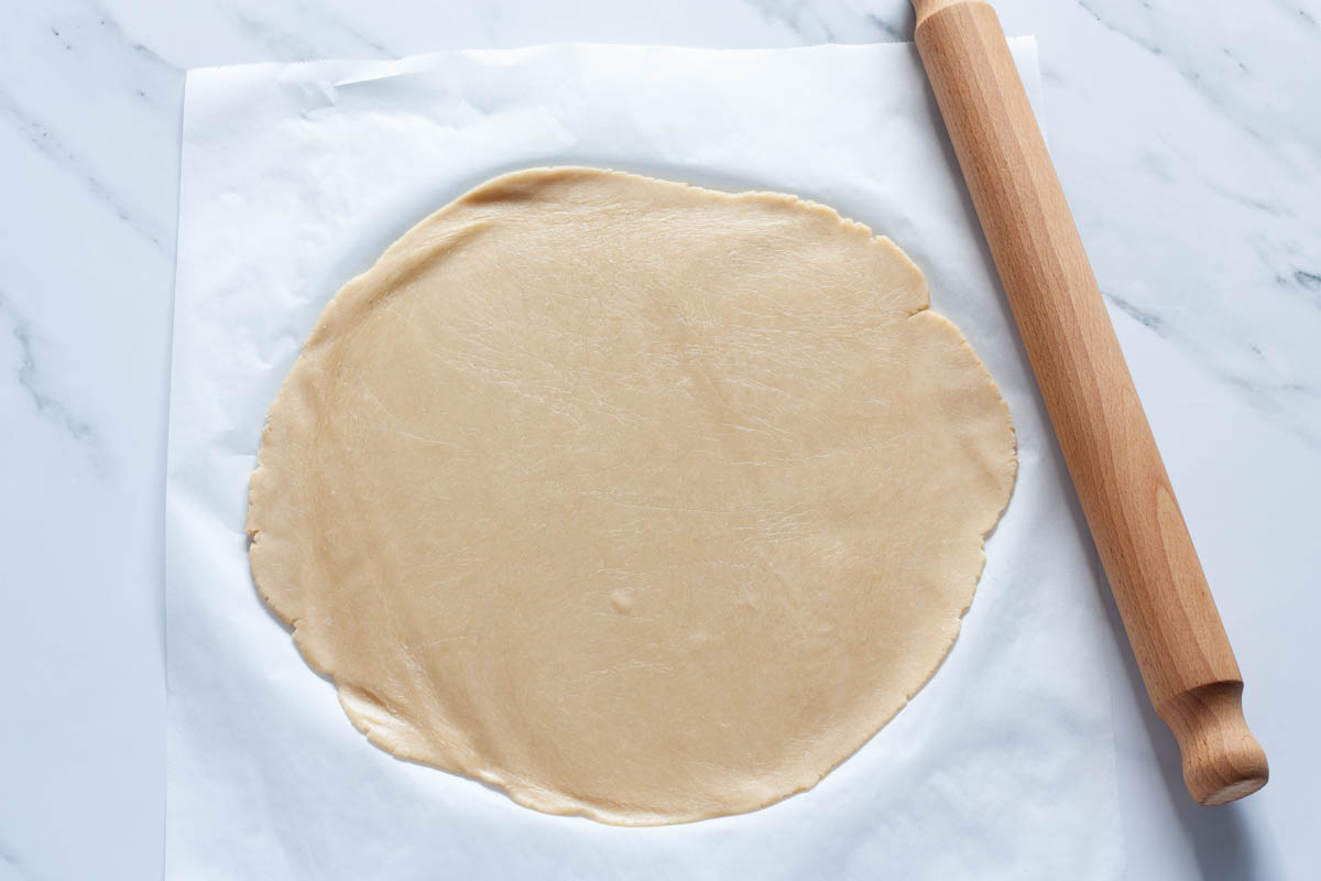 Rolled out tart dough on parchment paper next to a rolling pin.