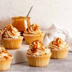 Caramel filled cupcakes on a white plate and a gray surface next to a jar of caramel sauce.