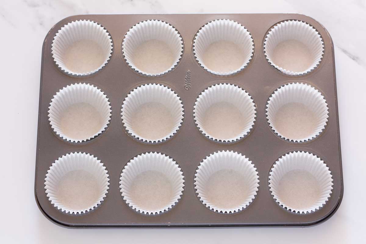 A cupcake pan lined with white cupcake liners.
