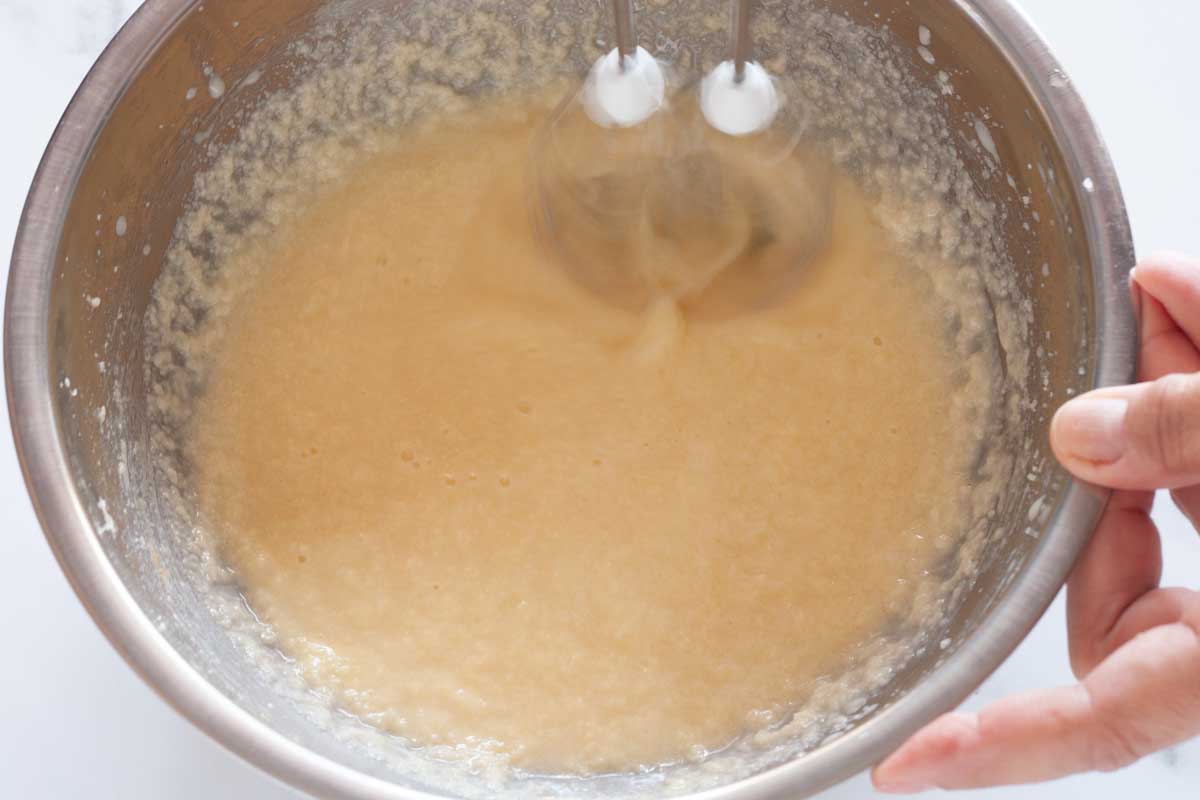 Beating buttermilk into egg and butter mixture with a hand mixer in a metal bowl.