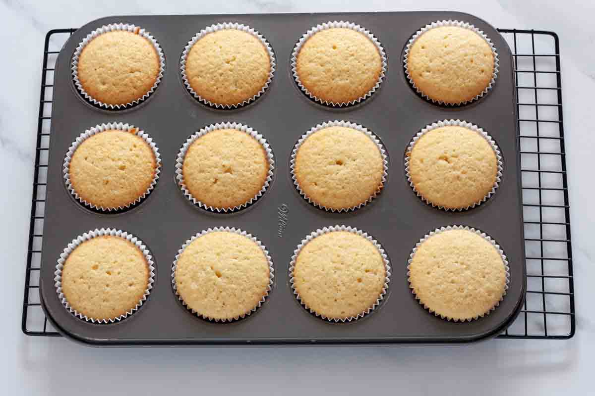Baked vanilla cookies in a cupcake pan on a wire rack.