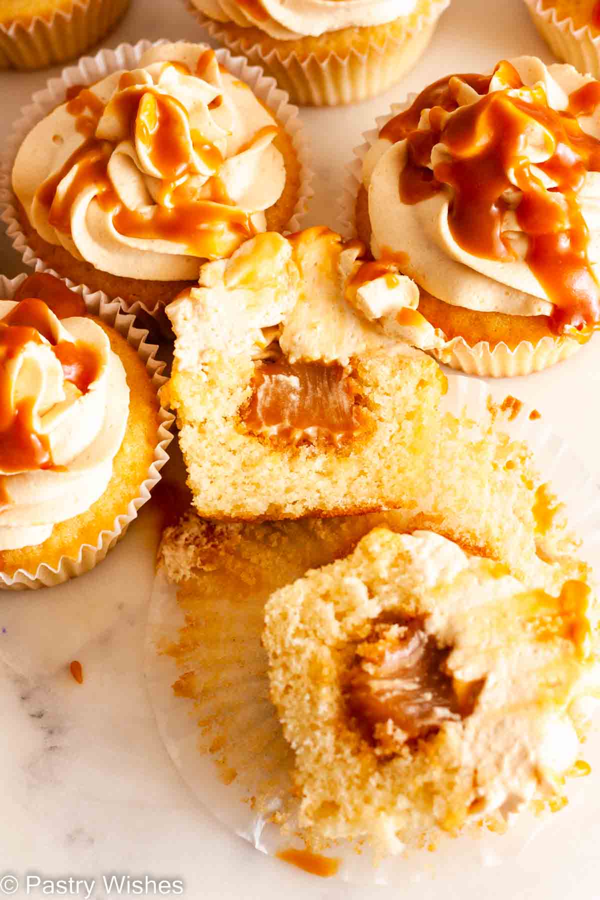 Caramel filled cupcakes on a white surface with a cupcake cut in half.