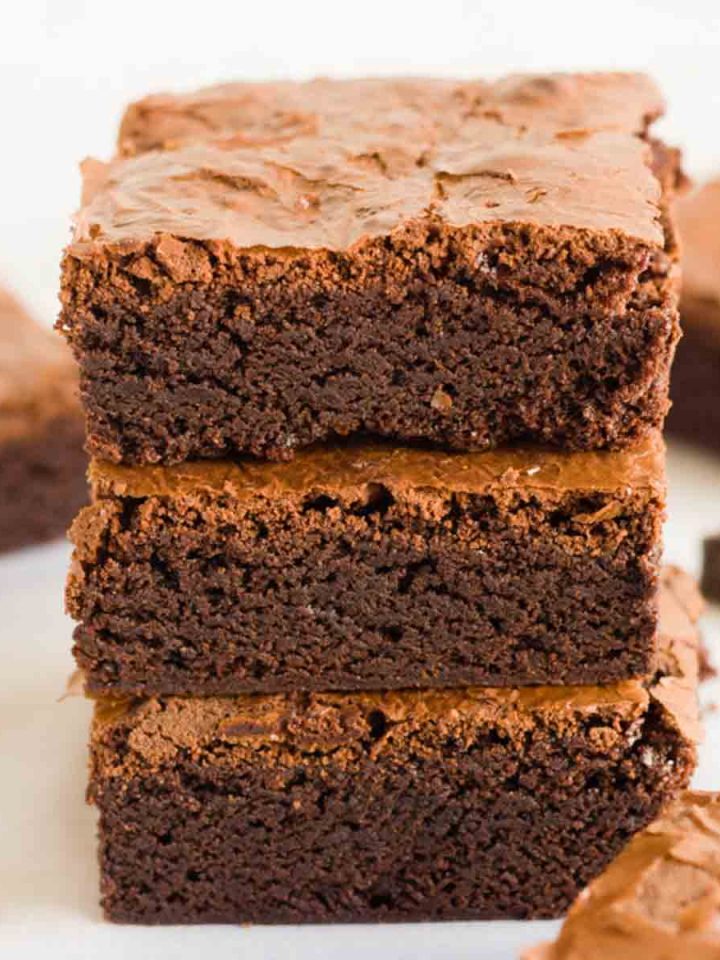 A stack of three classic homemade brownie squares next to chunks of chocolate and brownies.