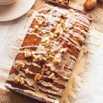 Overhead shot of a coffee and walnut loaf drizzled with coffee glaze on a brown surface.