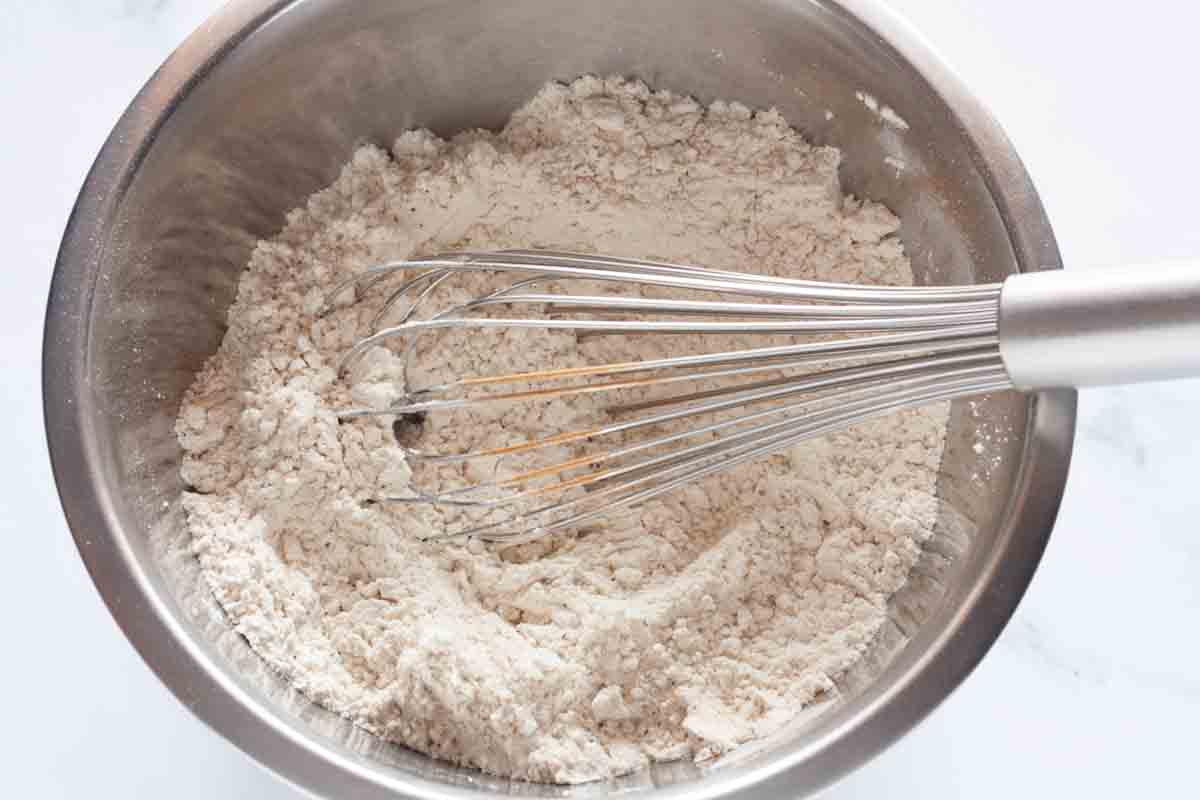 Whisking flour and other dry ingredients in a large metal mixing bowl.