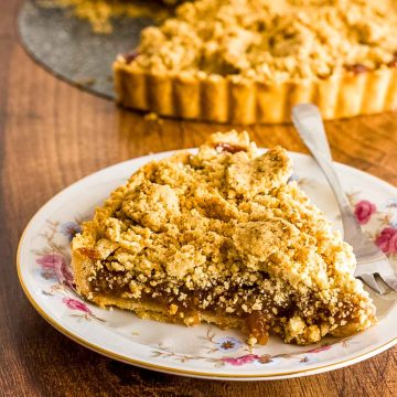 A slice of fig crumble tart on a plate with fig crumble tart in the background.