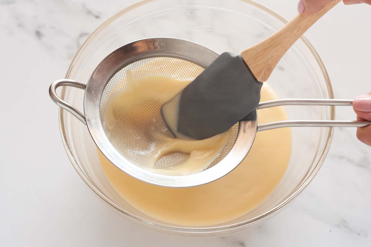 Straining the pastry cream through a strainer over a bowl with a rubber spatula.