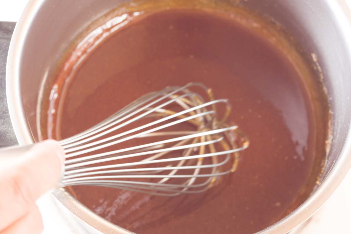 Stirring melted sugar in a metal saucepan with a whisk.