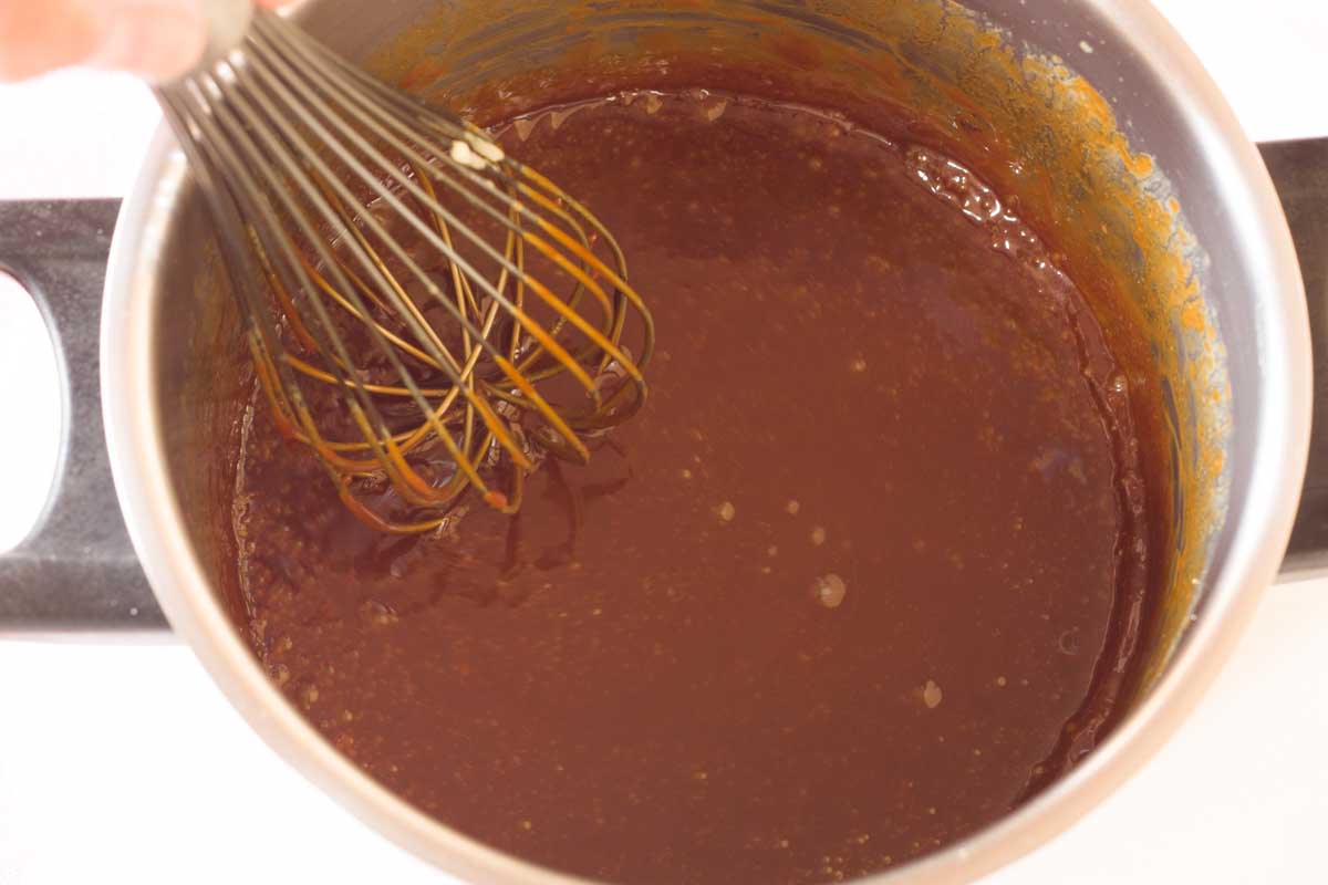 Whisking caramel sauce in a metal saucepan.