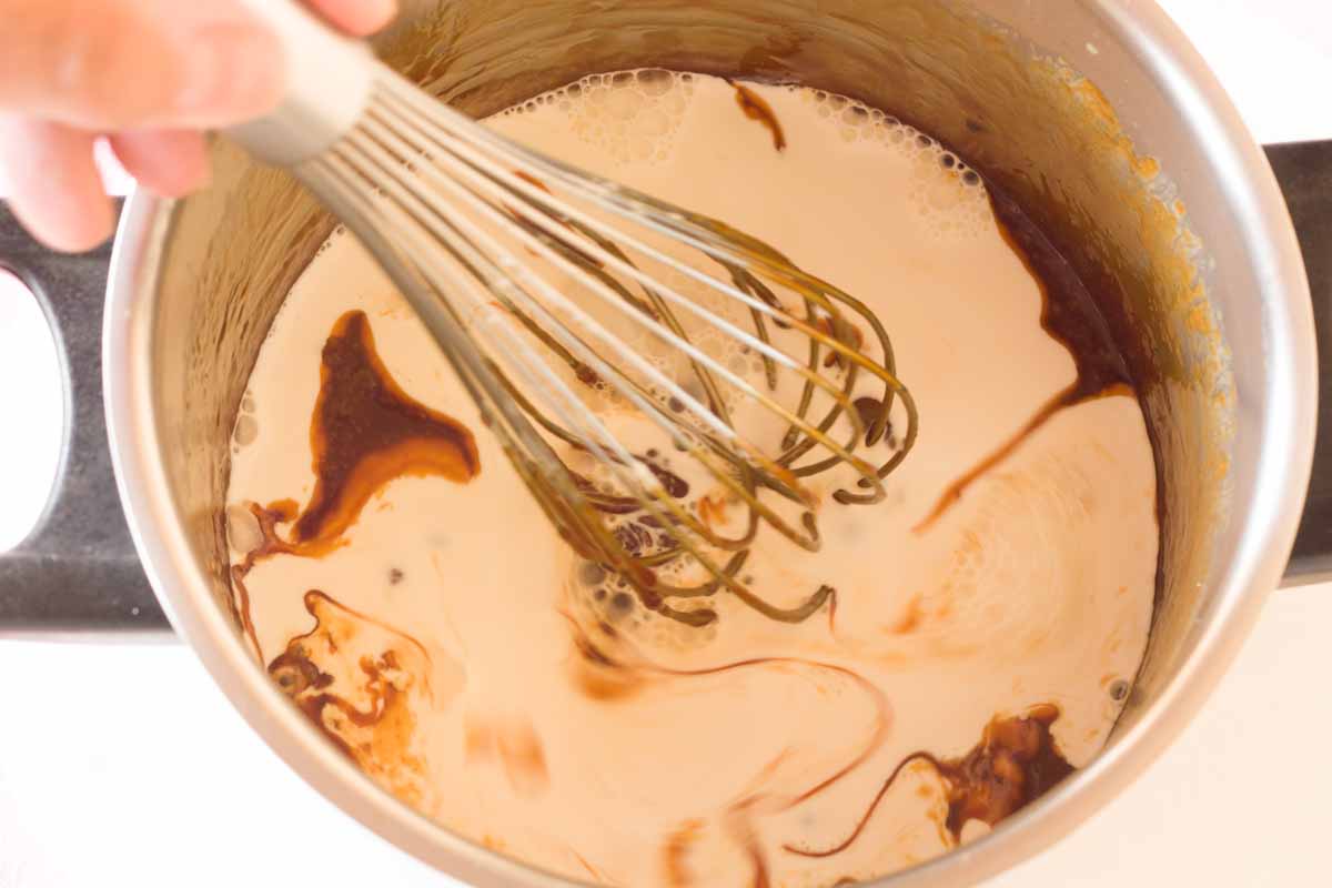 Whisking heavy cream into caramel with a whisk.