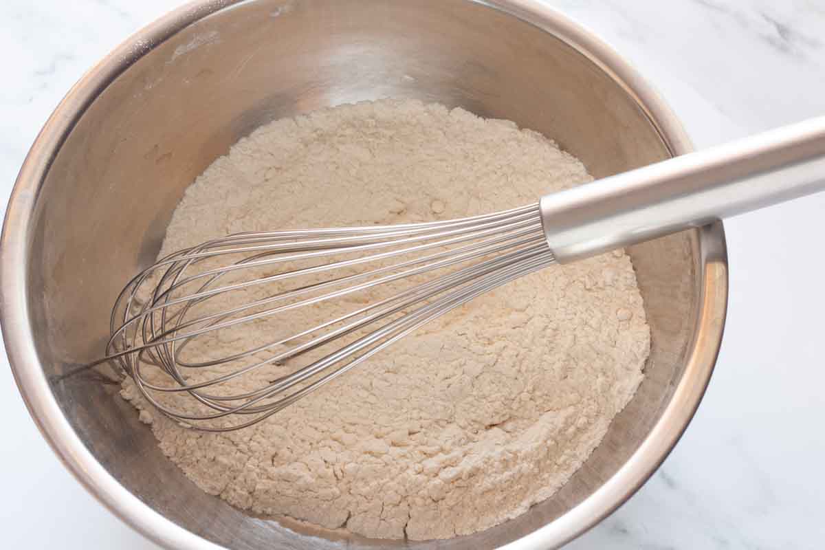 Whisking flour, baking powder, salt and cinnamon in a metal bowl.