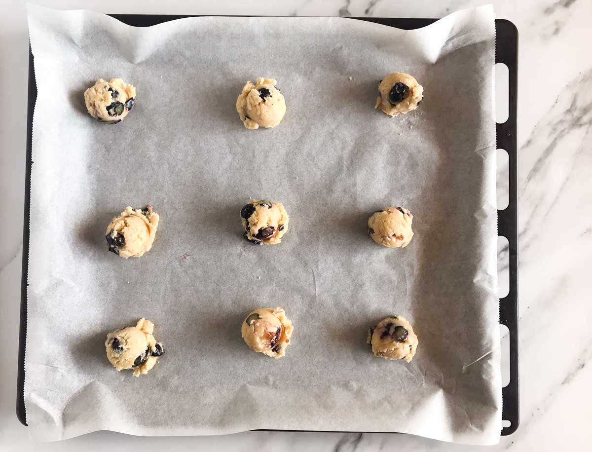 Nine unbaked lemon blueberry cookie dough balls on a baking sheet lined with parchment paper.