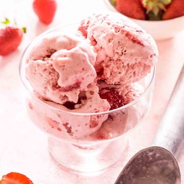 No churn strawberry ice cream in a glass bowl on a pink surface.