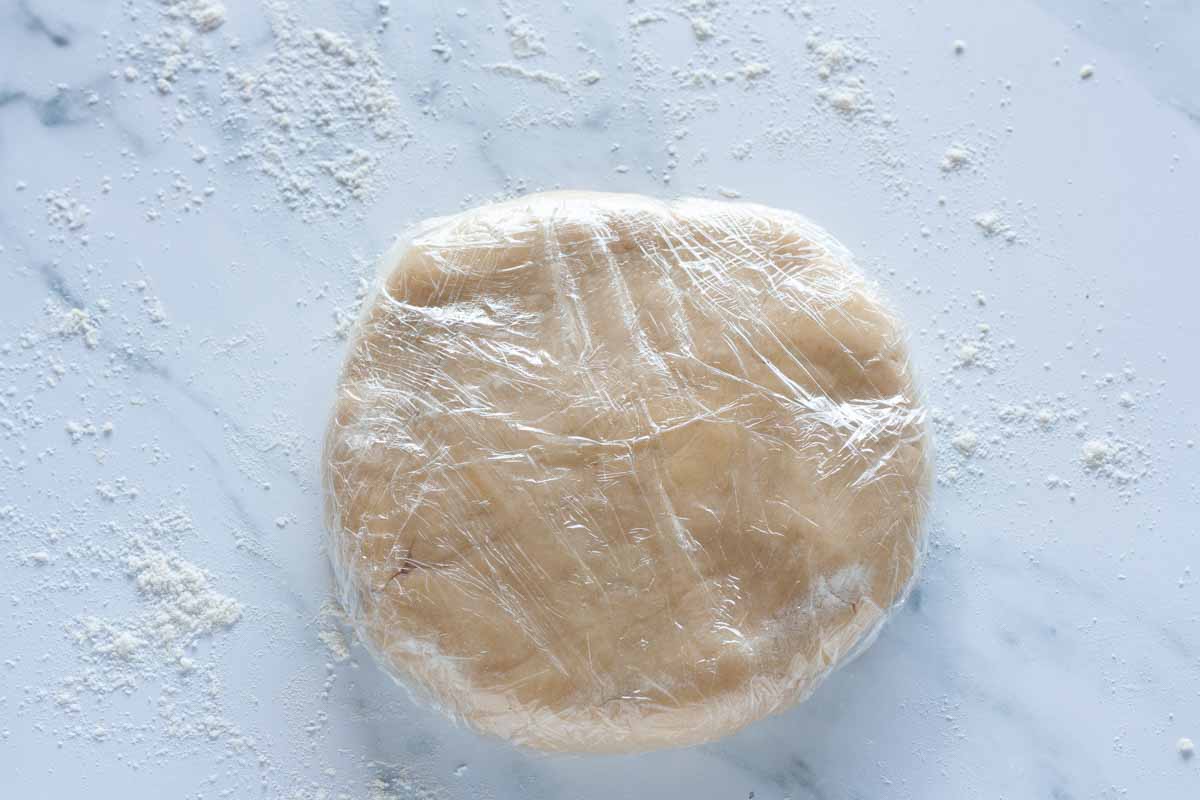 Tart dough flattened into a disk and wrapped in plastic wrap on a surface that's lightly floured.