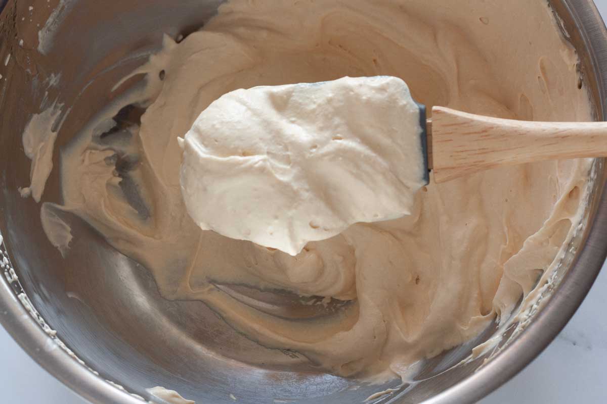 Stabilized caramel whipped cream on a spatula over a metal bowl.