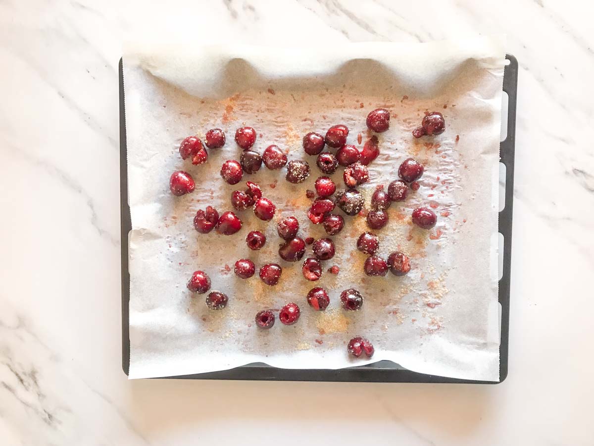 Fresh pitted cherries sprinkled with light brown sugar on a tray lined with parchment paper.