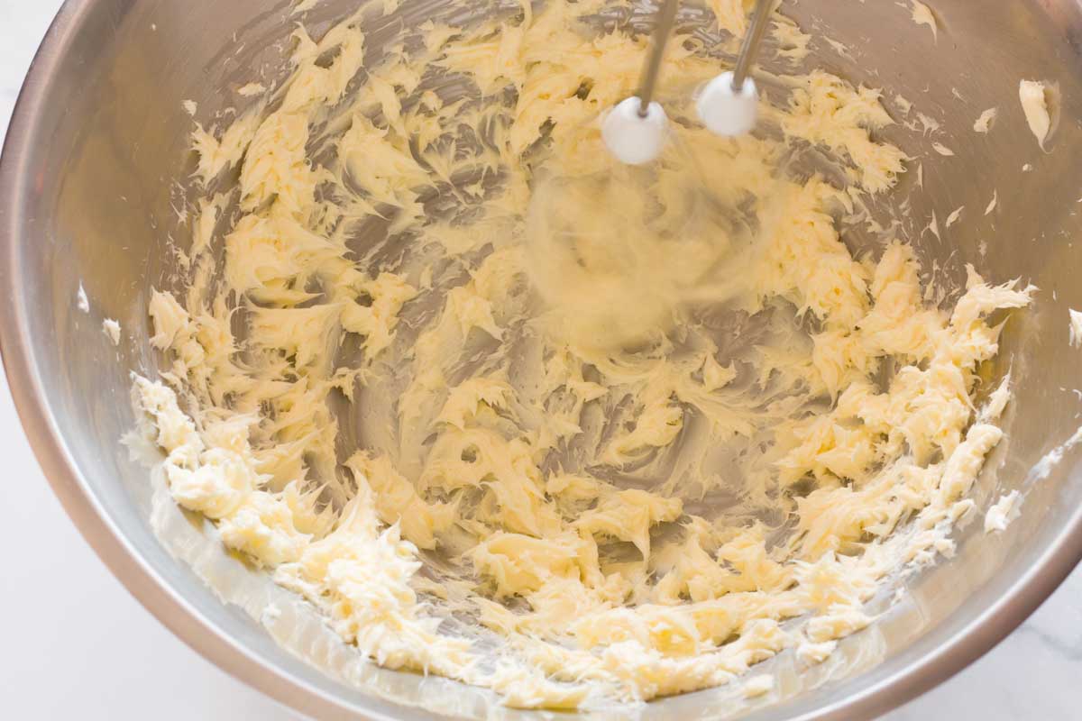 Beating butter until it's smooth in a metal mixing bowl with a hand mixer.