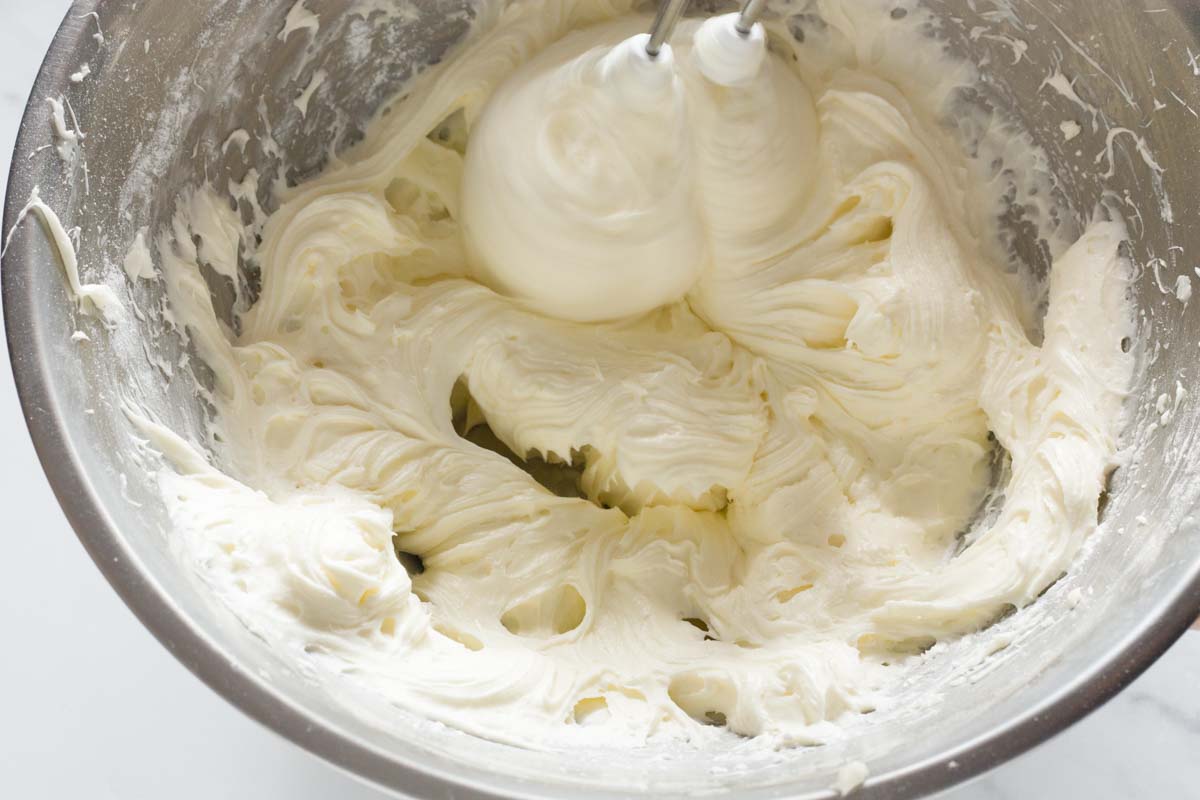 Beating cream cheese and vanilla with butter and sugar in a metal bowl with a hand mixer.