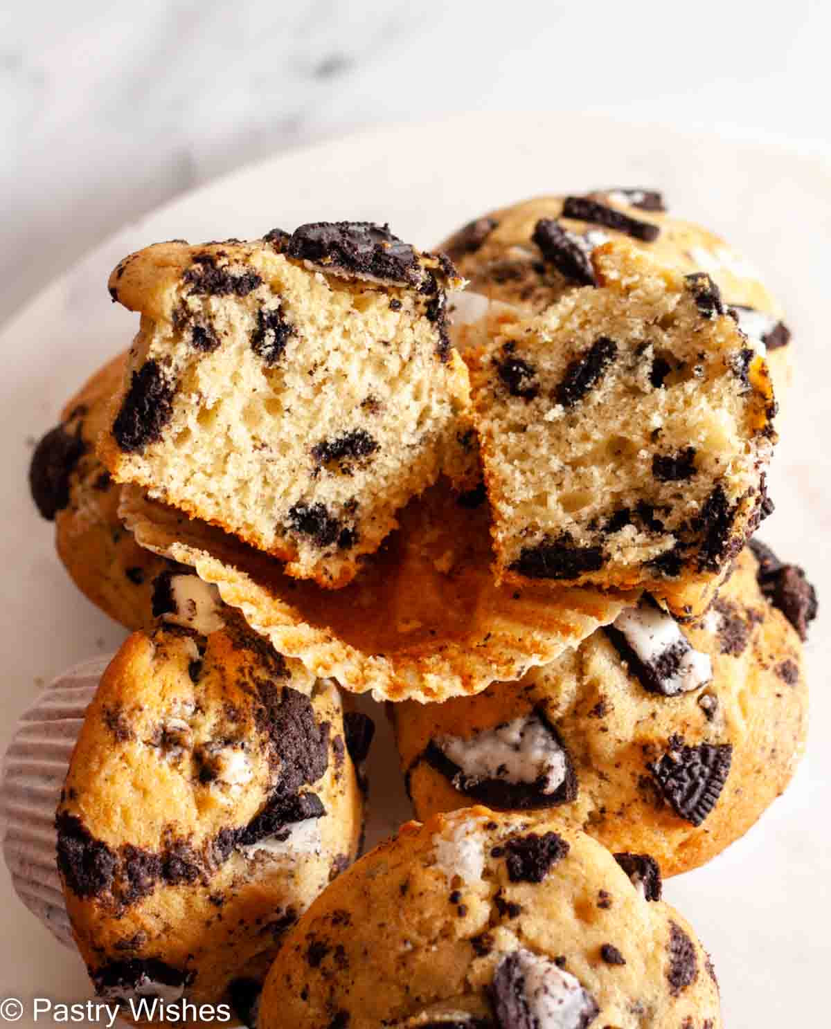 An Oreo muffin cut in half on top of three Oreo muffins on a white surface.