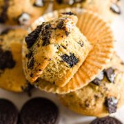 A closeup of an Oreo muffin on an unwrapped paper liner on top of four Oreo muffins and Oreo cookies.