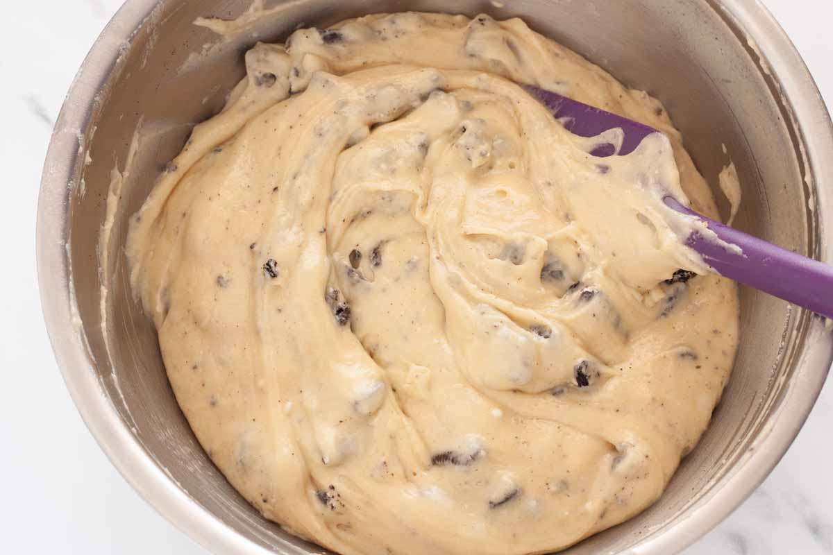 Folding crushed Oreo cookies in Oreo muffin batter in a metal bowl.