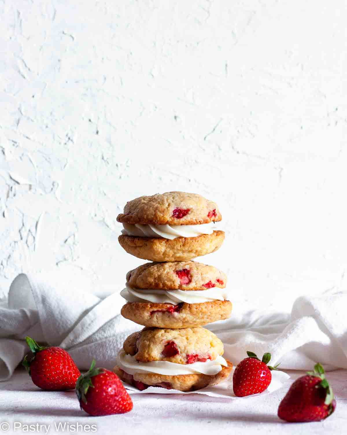 A stack of three strawberry cheesecake cookies on parchment paper next to strawberries and a white napkin.