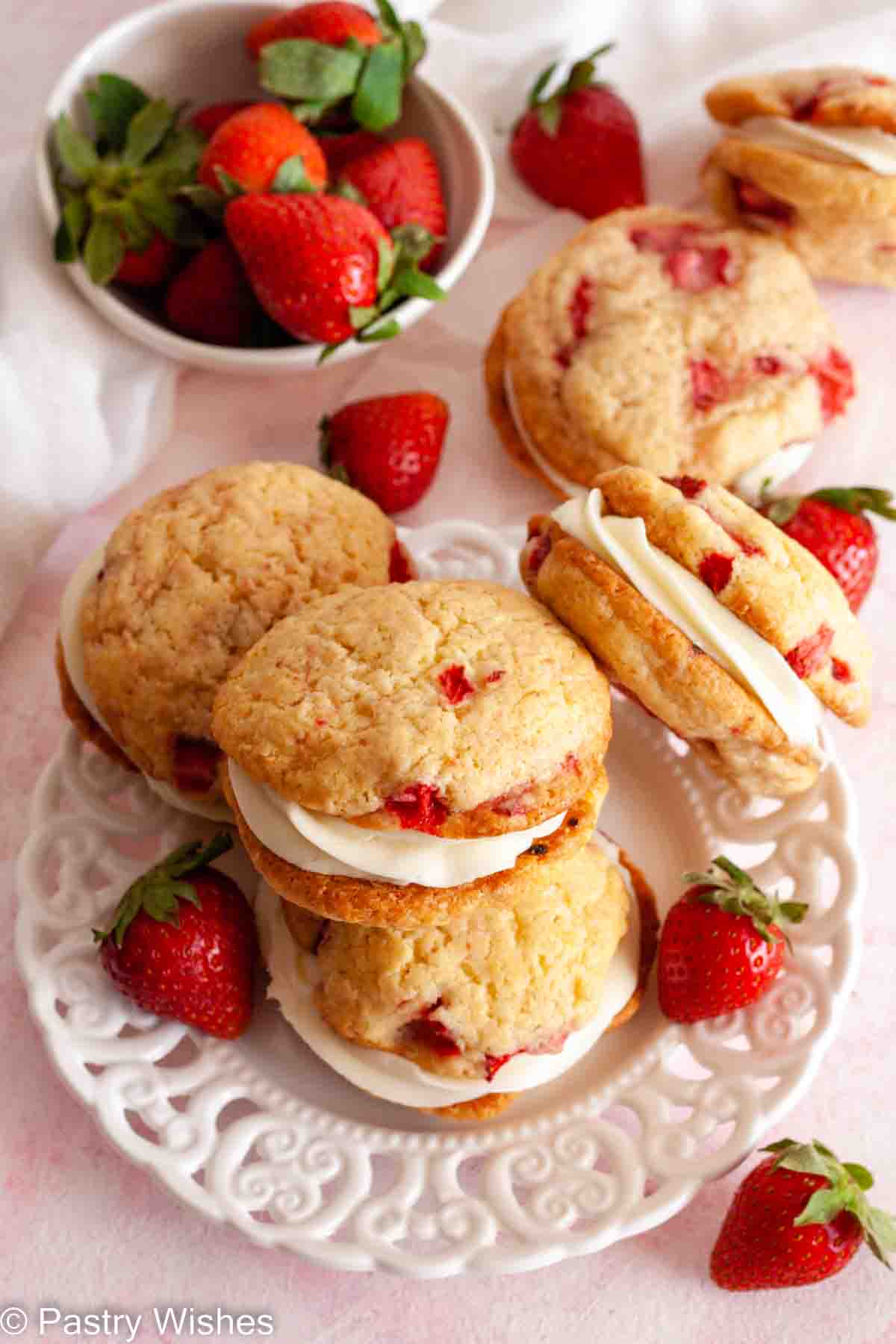 An overhead photo of strawberry cheesecake cookies on a white plate next to a bowl of strawberries.