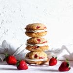 A stack of three strawberry cheesecake cookies on parchment paper next to strawberries and a white napkin.
