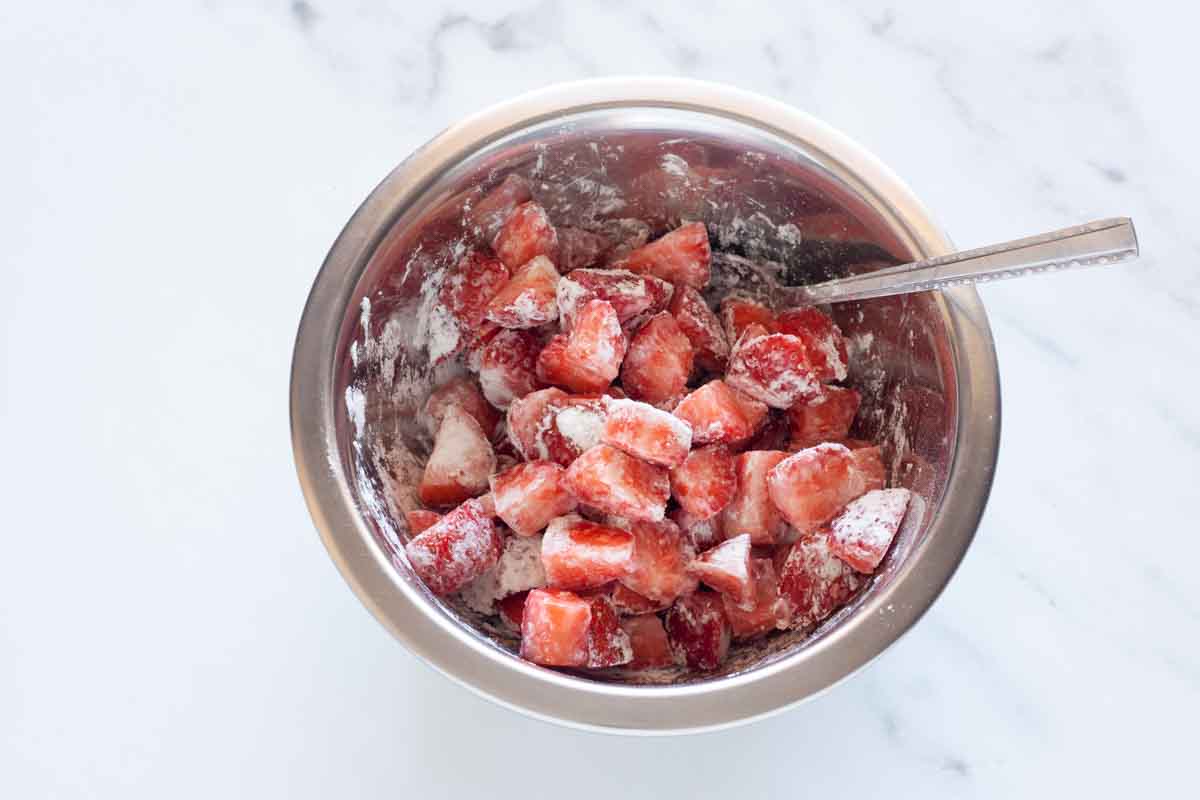Diced strawberries coated with cornstarch in a metal bowl with a spoon.
