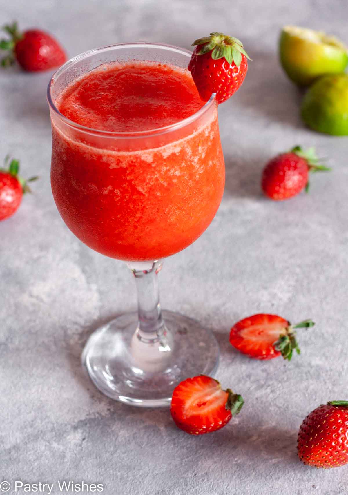 A strawberry daiquiri mocktail next to strawberries and limes.