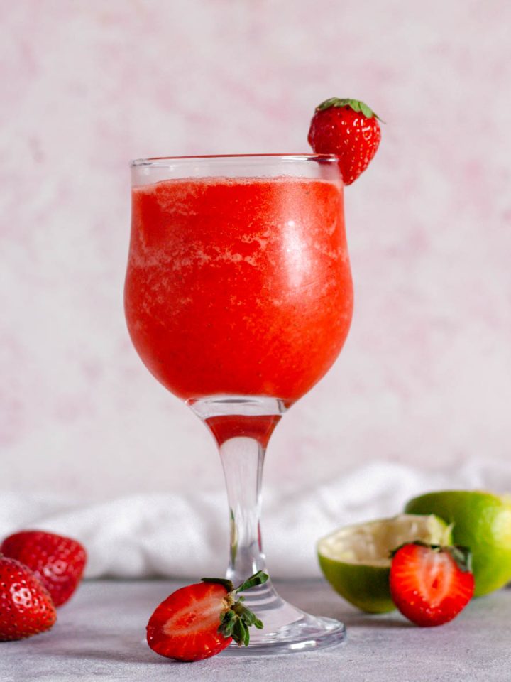 A closeup of a strawberry daiquiri mocktail next to strawberries and limes.