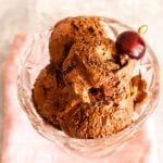 Four scoops of black forest ice cream in a glass bowl topped with a cherry.
