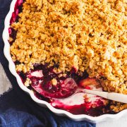 A closeup of baked blueberry apple crumble in a white baking dish with a spoon.