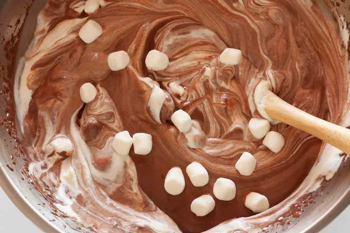 Folding whipped cream and mini marshmallows with chocolate mixture with a spatula.
