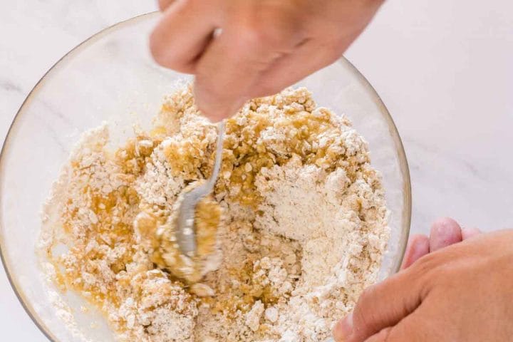 Stirring melted butter with flour, old-fashioned oats and spices in a glass bowl.