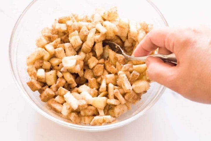 Stirring apple pie filling in a glass bowl with a spoon.
