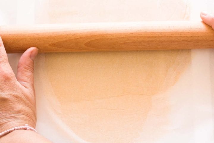 Rolling out pie dough between two sheets of parchment paper with a rolling pin.