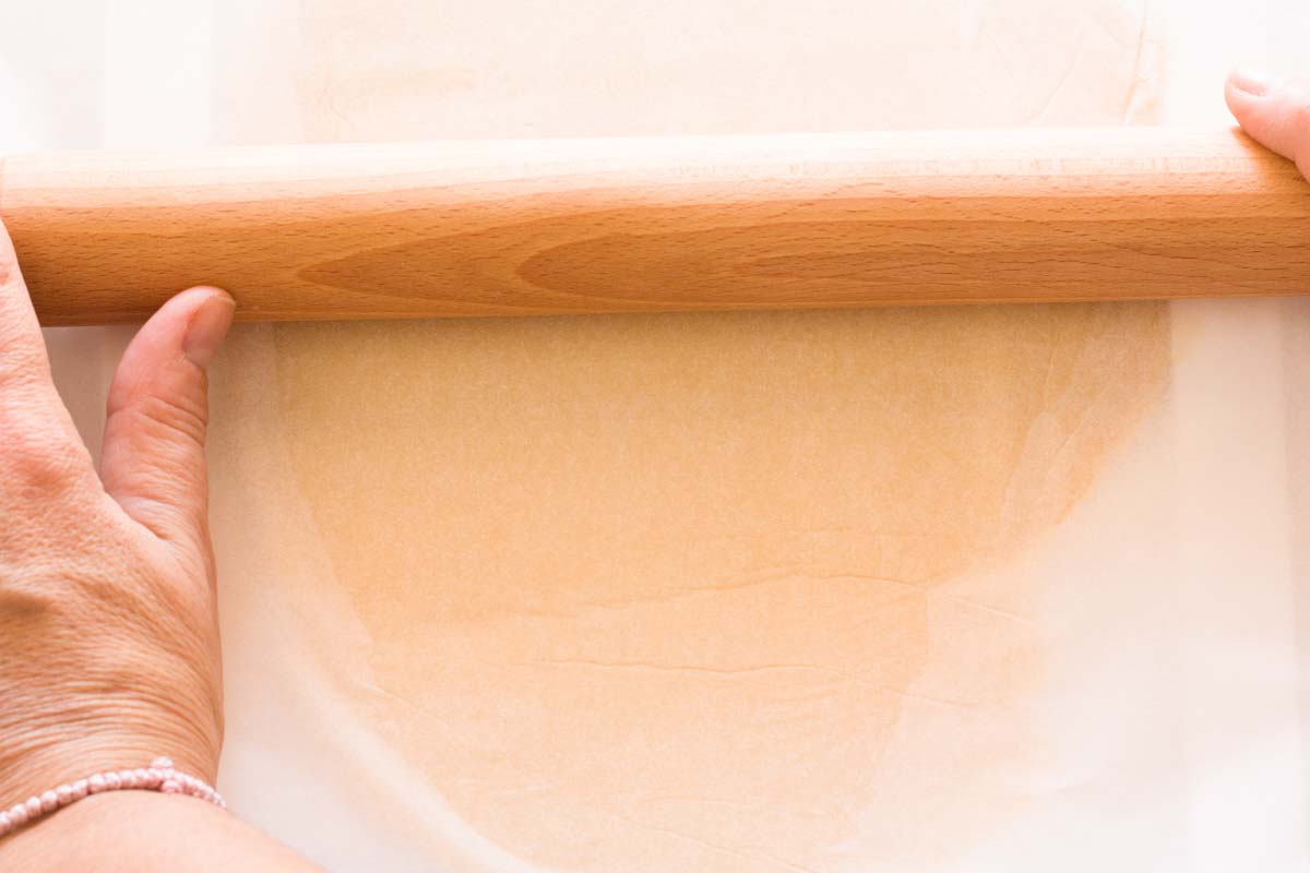 Rolling out pie dough between two sheets of parchment paper with a rolling pin.