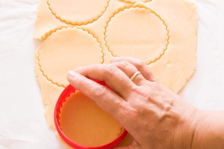 A hand cutting out circles of dough with a fluted cookie cutter.