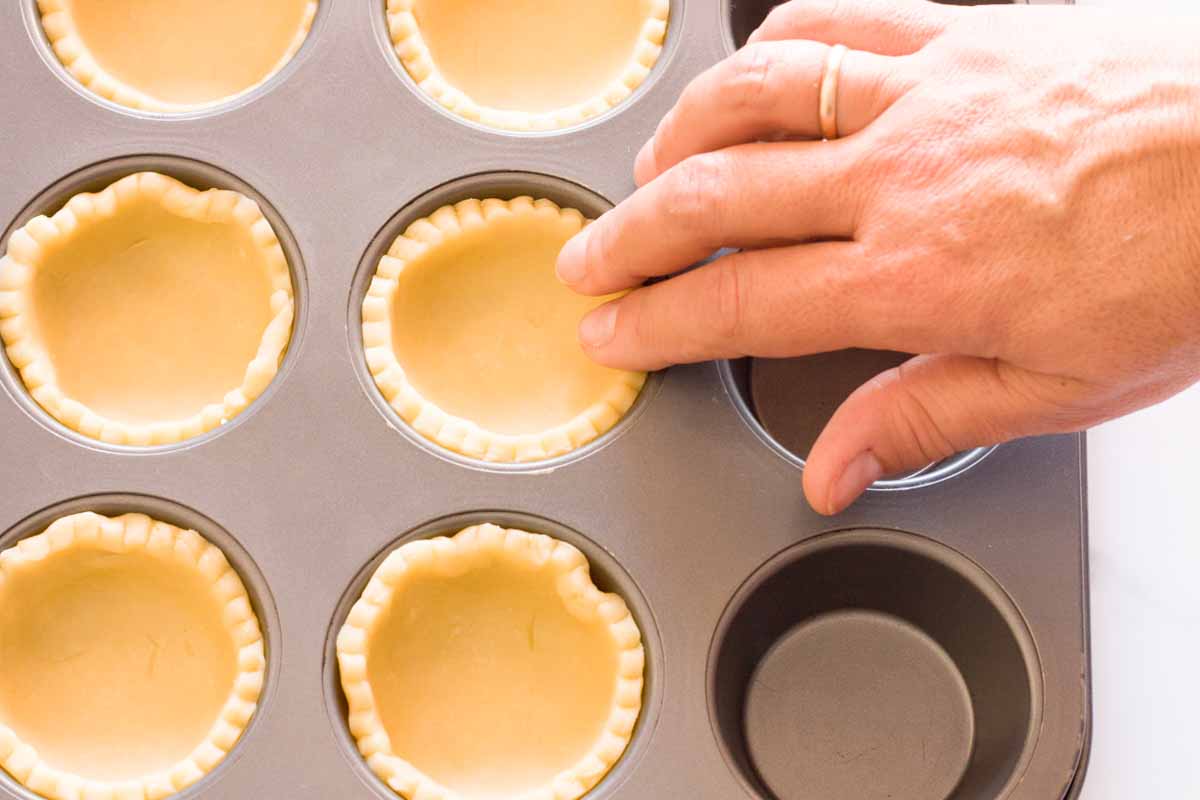A hand placing cut out circles of pie dough into a cupcake pan.