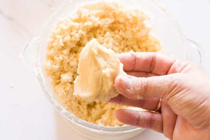 A hand holding together a piece of dough that has come together in a food processor.