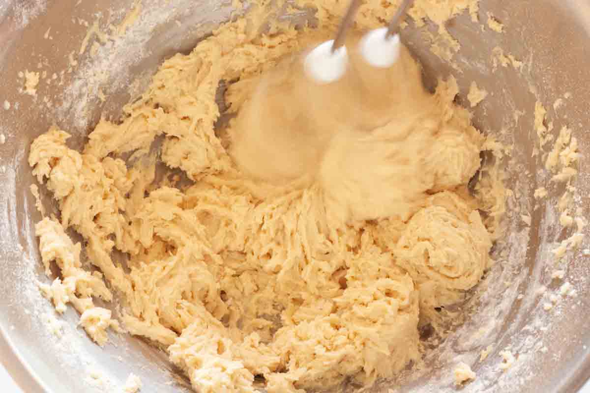 Adding flour to butter mixture in a metal mixing bowl with a hand mixer.