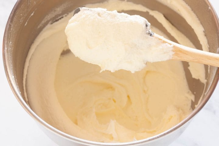 A closeup of smooth vanilla buttercream frosting on a rubber spatula over a bowl of a stand mixer.